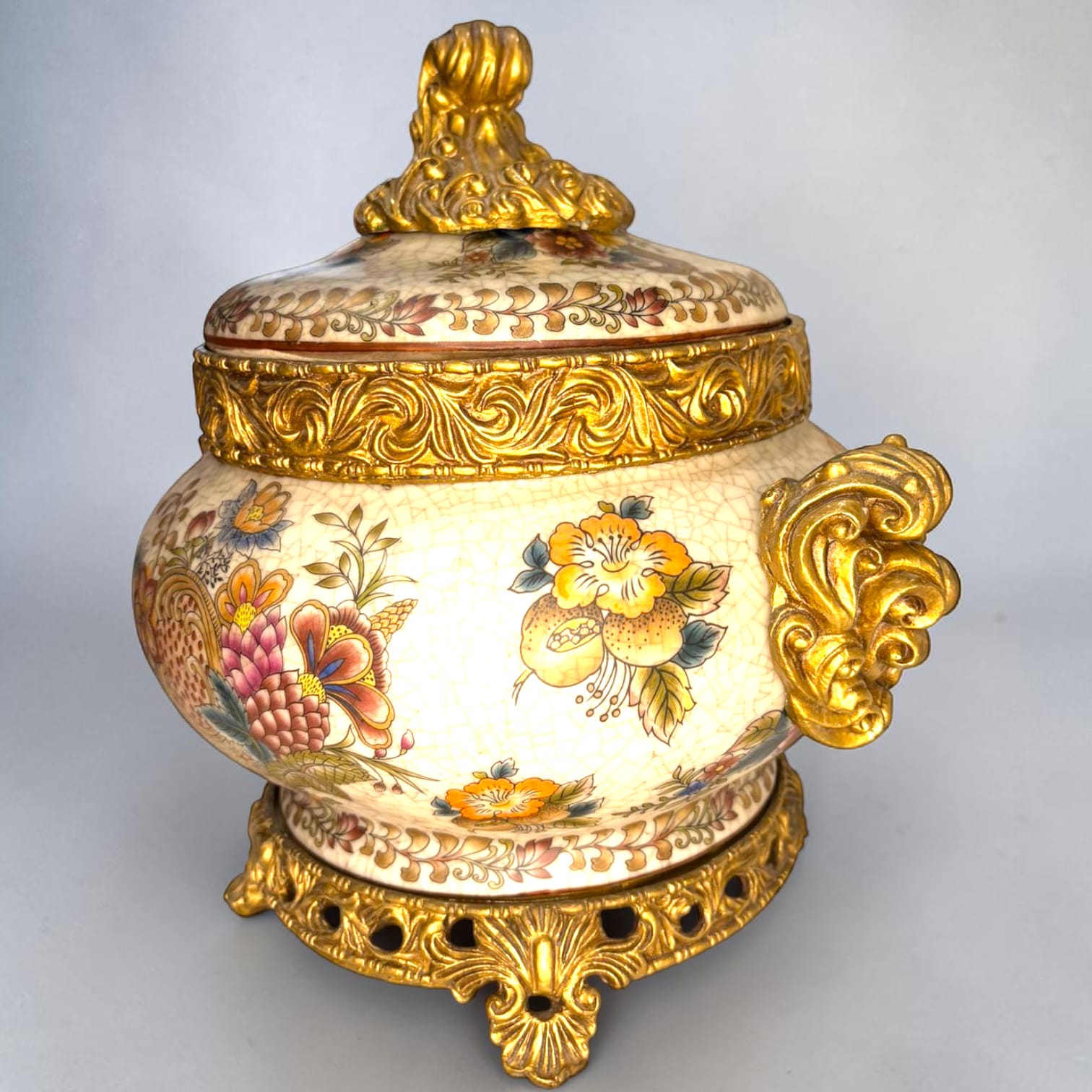 Formado por tres recipientes ornamentales con tapa, combina fondo marfil craquelado, motivos florales multicolor y relieves dorados de gran impacto visual.

Su función original es guardar joyas, pequeños recuerdos, bisutería, llaves, medallas o piezas delicadas. Hoy también destaca como objeto decorativo y de colección, ideal para vitrinas, tocadores, apar