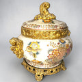 Formado por tres recipientes ornamentales con tapa, combina fondo marfil craquelado, motivos florales multicolor y relieves dorados de gran impacto visual.

Su función original es guardar joyas, pequeños recuerdos, bisutería, llaves, medallas o piezas delicadas. Hoy también destaca como objeto decorativo y de colección, ideal para vitrinas, tocadores, apar