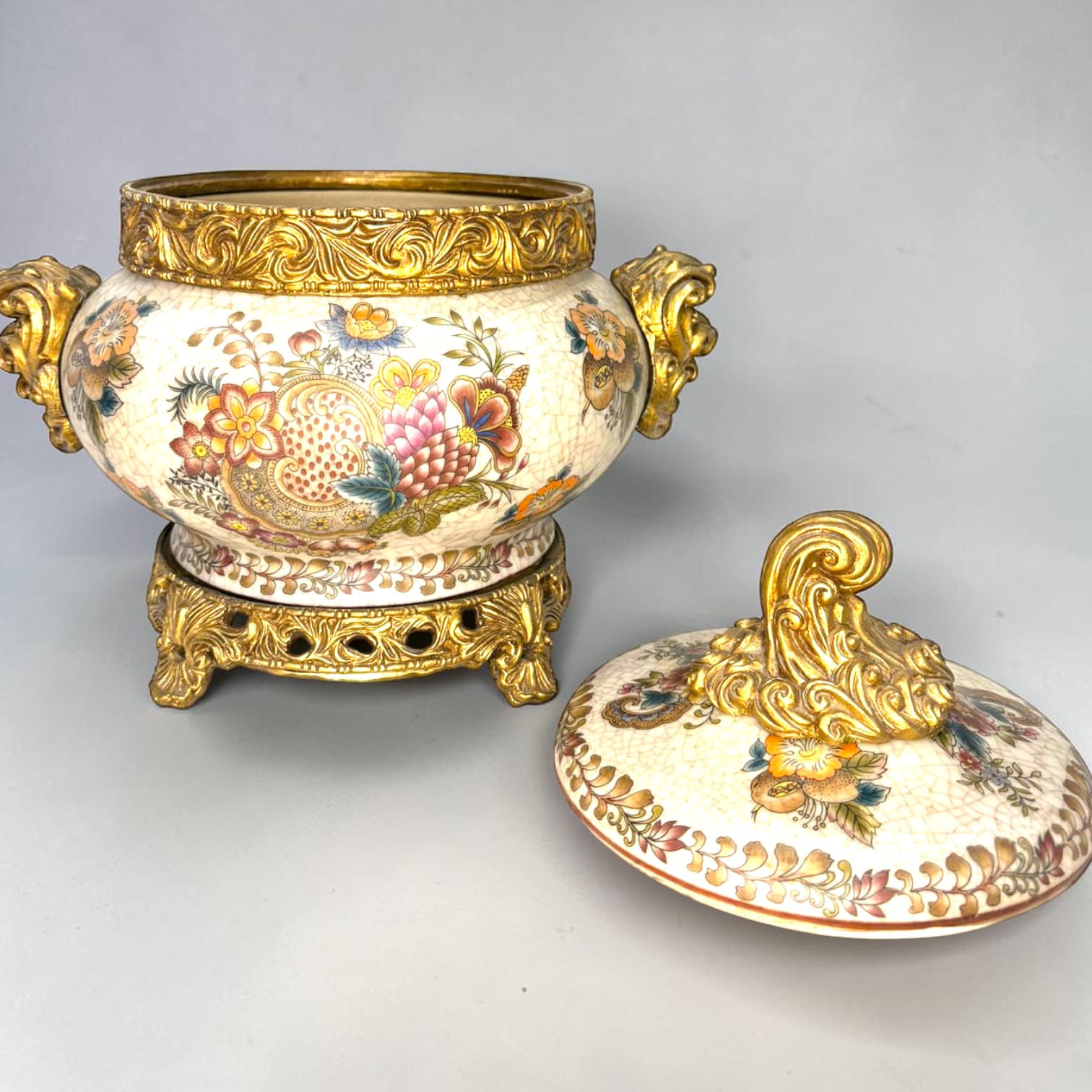 Formado por tres recipientes ornamentales con tapa, combina fondo marfil craquelado, motivos florales multicolor y relieves dorados de gran impacto visual.

Su función original es guardar joyas, pequeños recuerdos, bisutería, llaves, medallas o piezas delicadas. Hoy también destaca como objeto decorativo y de colección, ideal para vitrinas, tocadores, apar