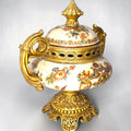 Formado por tres recipientes ornamentales con tapa, combina fondo marfil craquelado, motivos florales multicolor y relieves dorados de gran impacto visual.

Su función original es guardar joyas, pequeños recuerdos, bisutería, llaves, medallas o piezas delicadas. Hoy también destaca como objeto decorativo y de colección, ideal para vitrinas, tocadores, apar