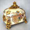 Formado por tres recipientes ornamentales con tapa, combina fondo marfil craquelado, motivos florales multicolor y relieves dorados de gran impacto visual.

Su función original es guardar joyas, pequeños recuerdos, bisutería, llaves, medallas o piezas delicadas. Hoy también destaca como objeto decorativo y de colección, ideal para vitrinas, tocadores, apar