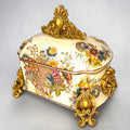 Formado por tres recipientes ornamentales con tapa, combina fondo marfil craquelado, motivos florales multicolor y relieves dorados de gran impacto visual.

Su función original es guardar joyas, pequeños recuerdos, bisutería, llaves, medallas o piezas delicadas. Hoy también destaca como objeto decorativo y de colección, ideal para vitrinas, tocadores, apar