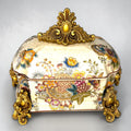 Formado por tres recipientes ornamentales con tapa, combina fondo marfil craquelado, motivos florales multicolor y relieves dorados de gran impacto visual.

Su función original es guardar joyas, pequeños recuerdos, bisutería, llaves, medallas o piezas delicadas. Hoy también destaca como objeto decorativo y de colección, ideal para vitrinas, tocadores, apar