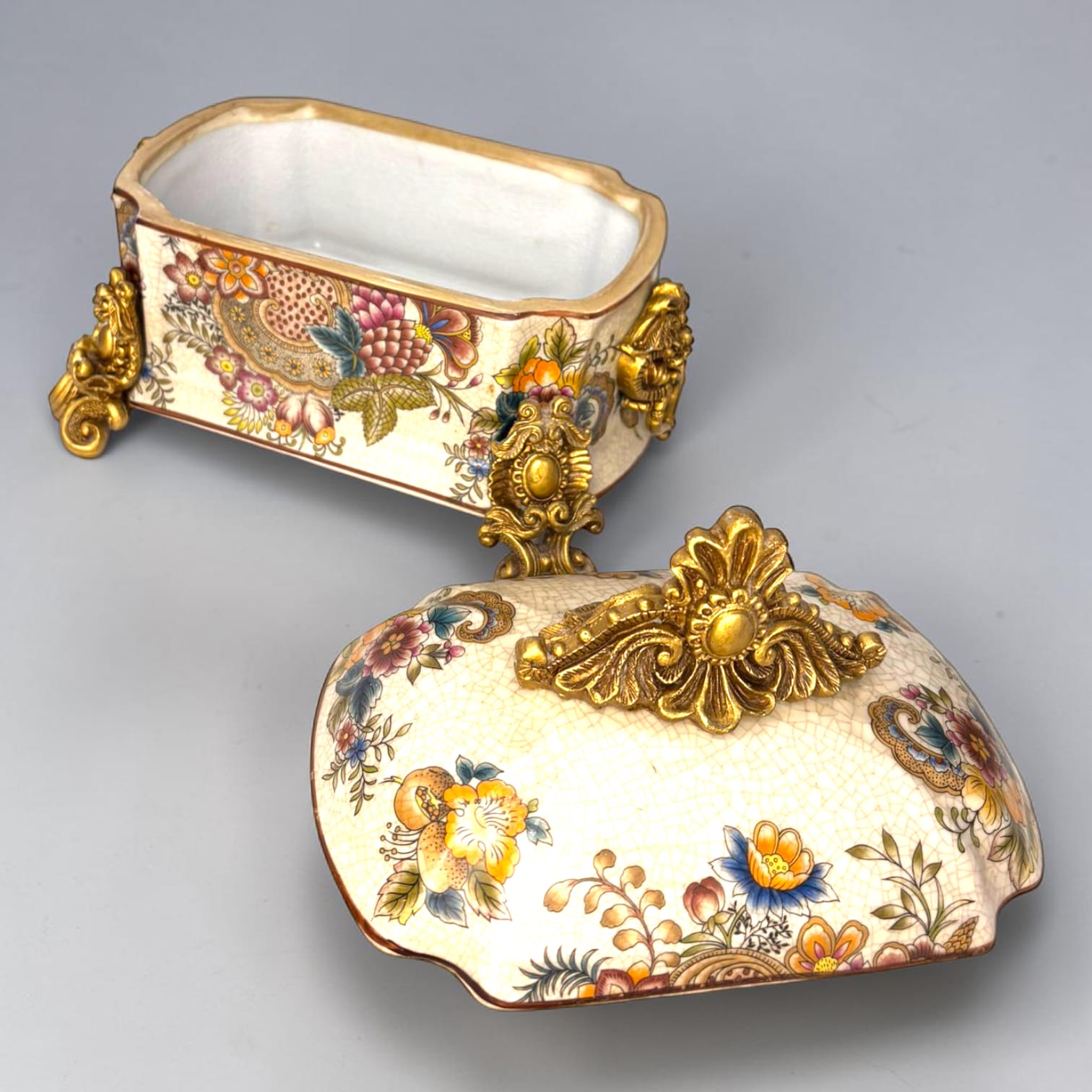 Formado por tres recipientes ornamentales con tapa, combina fondo marfil craquelado, motivos florales multicolor y relieves dorados de gran impacto visual.

Su función original es guardar joyas, pequeños recuerdos, bisutería, llaves, medallas o piezas delicadas. Hoy también destaca como objeto decorativo y de colección, ideal para vitrinas, tocadores, apar