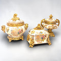 Formado por tres recipientes ornamentales con tapa, combina fondo marfil craquelado, motivos florales multicolor y relieves dorados de gran impacto visual.

Su función original es guardar joyas, pequeños recuerdos, bisutería, llaves, medallas o piezas delicadas. Hoy también destaca como objeto decorativo y de colección, ideal para vitrinas, tocadores, apar