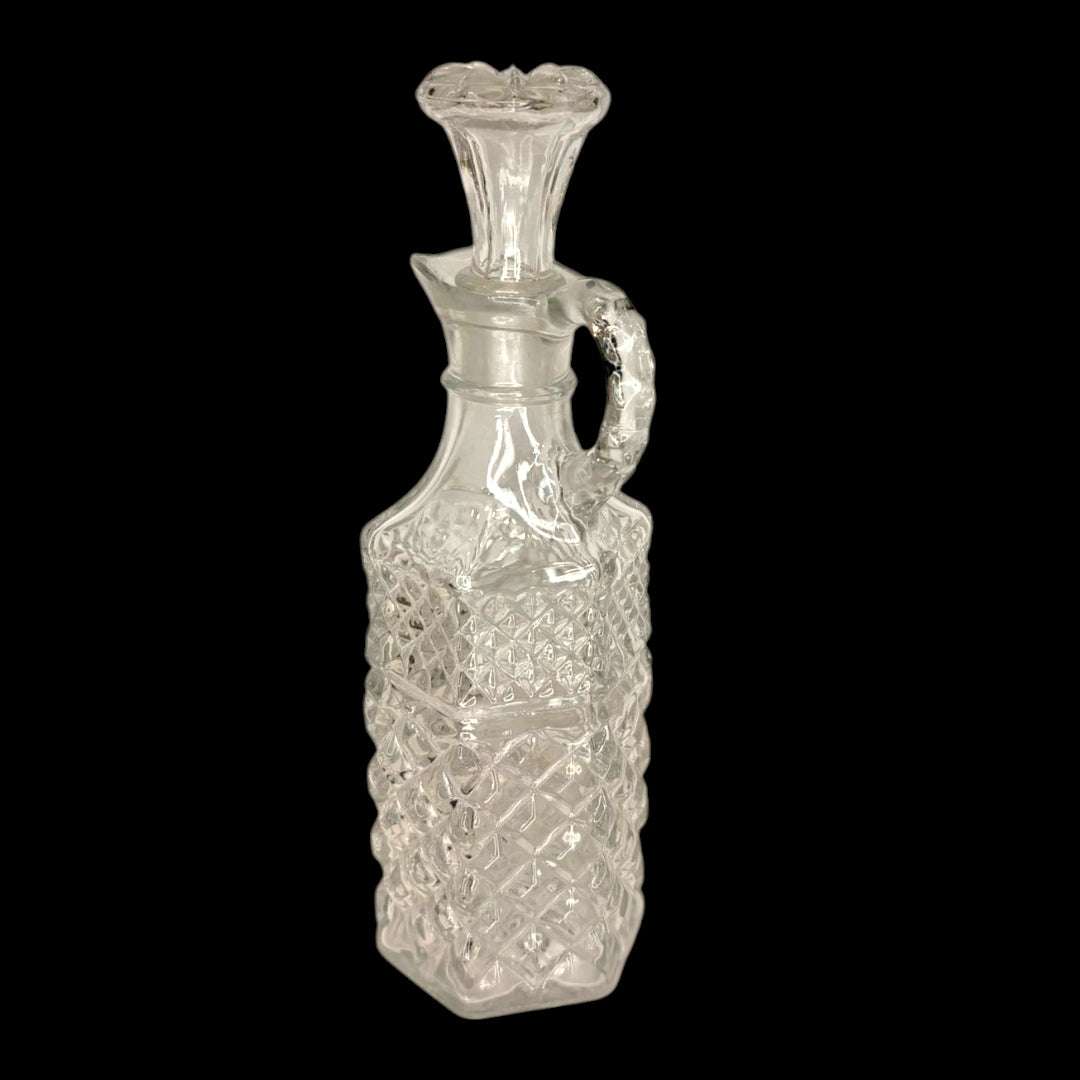 Su diseño con asa lateral, pico vertedor y tapón de cristal refleja el gusto por los servicios de mesa cuidados, donde cada detalle aportaba presencia y distinción.