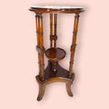 Estos Veladores destacan por una estructura muy original: tablero superior circular, columnas verticales decorativas y una pequeña repisa central que permite crear dos alturas de exposición. Esta repisa resulta perfecta para colocar una maceta con flores, una figura pequeña, una porcelana, una vela decorativa o un detalle especial, mientras que la parte superior puede utilizarse para una lámpara, un jarrón o una pieza protagonista.

En las imágenes se aprecia un acabado brillante de tono caoba cálido, con t