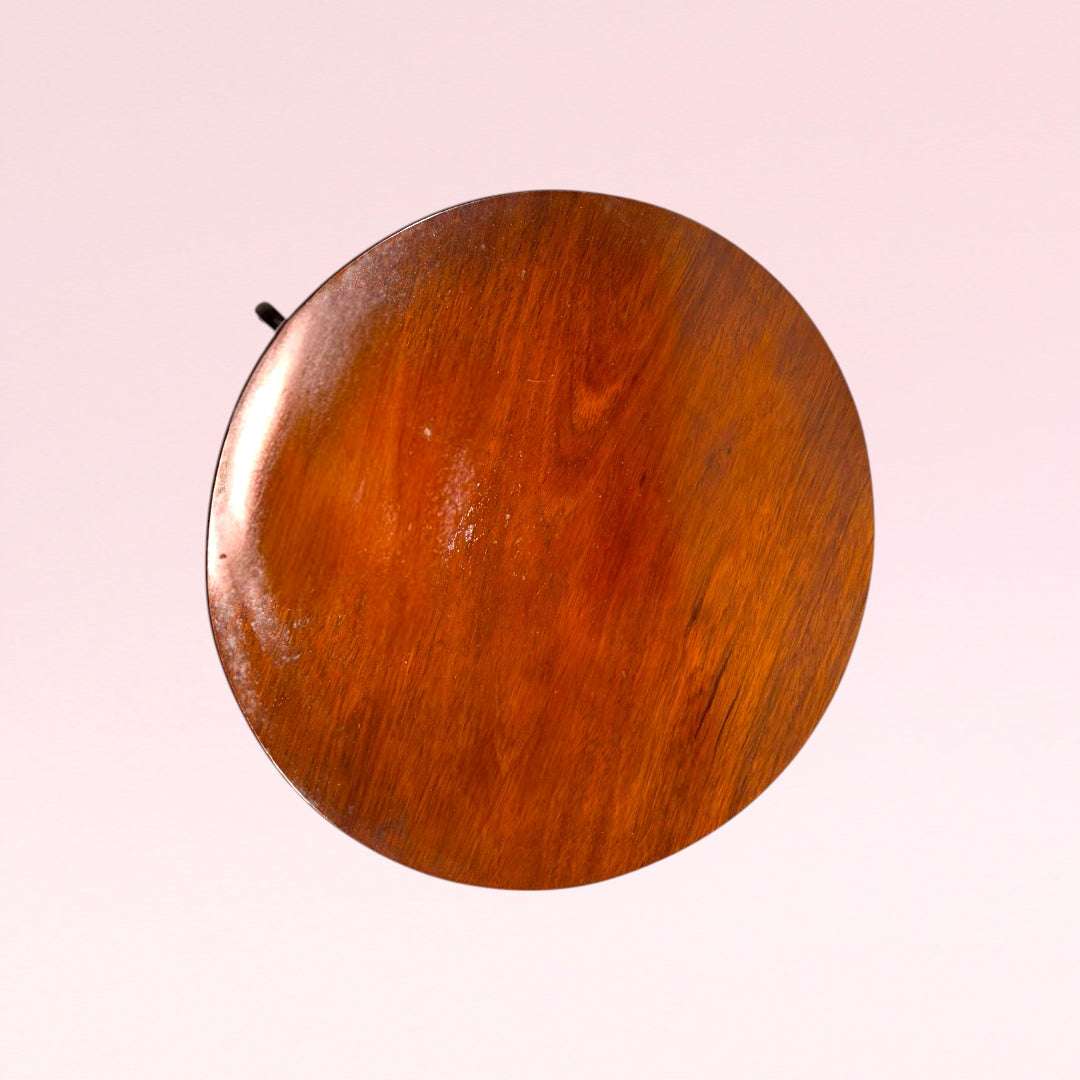 La combinación de tablero redondo, madera de caoba, pie central torneado, base de tres patas curvas y acabado cálido con brillo suave lo diferencia de una mesa auxiliar común.