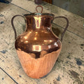  Realizada en cobre, presenta una silueta elegante y robusta, acompañada de tapa superior y dos asas laterales de hierro oscuro, que le aportan carácter y autenticidad.