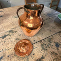  Realizada en cobre, presenta una silueta elegante y robusta, acompañada de tapa superior y dos asas laterales de hierro oscuro, que le aportan carácter y autenticidad.