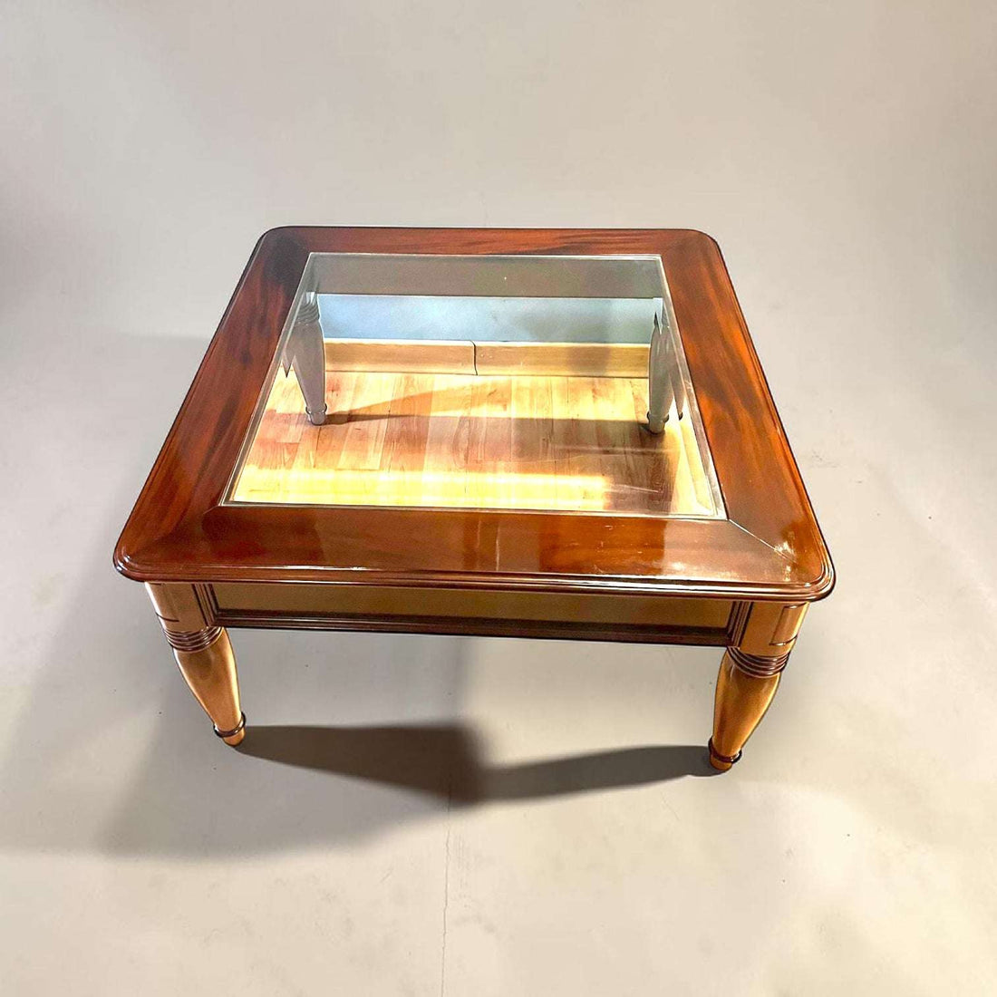 Elegante Mesa baja de salón realizada en madera de caoba, una pieza clásica y refinada que destaca por sus líneas equilibradas, su excelente presencia decorativa y su sofisticado cristal biselado central.