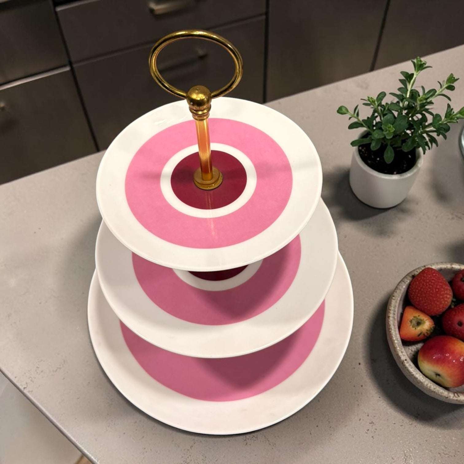 Compuesto por tres platos de porcelana en distintos tamaños y unidos mediante una estructura de metal dorado, destaca por su diseño sofisticado y su estética vintage con un aire muy especial.