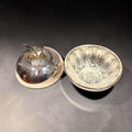 Su función original era conservar y presentar la mantequilla en la mesa, protegiéndola con su estructura cerrada y aportando al servicio un detalle elegante. 