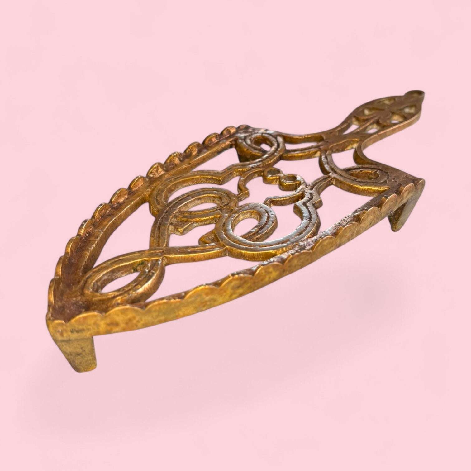 Este Descansadero destaca por su diseño calado, elegante y ornamental. Su estructura presenta formas curvas, motivos simétricos y una silueta alargada que recuerda a los antiguos soportes domésticos utilizados en tareas de planchado. 