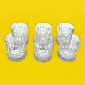 Seis vasos de cristal con patrón cuadriculado, juego decorativo que acompaña la coctelera con tapa de plata para eventos sofisticados.