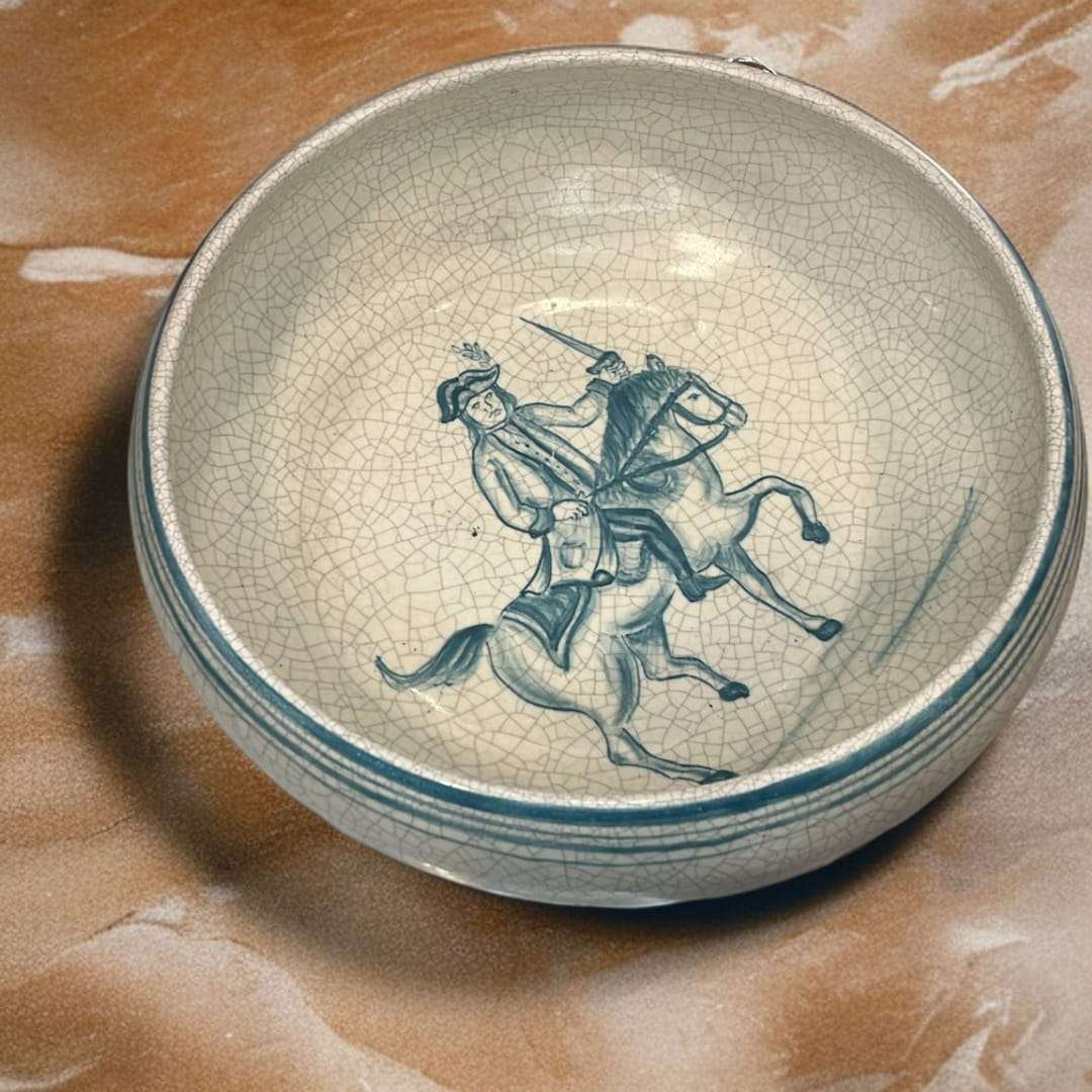 Detalle del plato artesanal con jinete pintado a mano en tonos azulados.