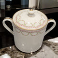 Azucarero de porcelana francesa con tapa y asas doradas, diseño clásico con detalles florales en rosa. Pieza decorativa para mesa distinguida.