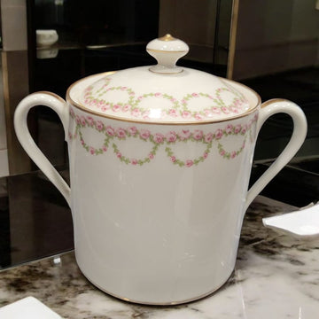 Azucarero de porcelana francesa con tapa y asas doradas, decorado con guirnaldas de rosas rosadas sobre fondo blanco. Ideal para decoración elegante.