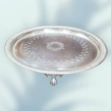 Bandeja de metal plateado con ornamentos elegantes, diseño floral en relieve y escudo central, ideal para decoración vintage de interiores.