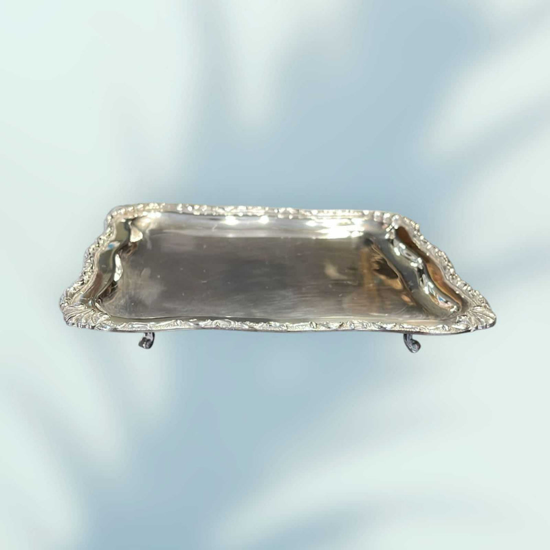 Bandeja de metal plateado con patas y bordes decorativos en forma cuadrada, ideal para decoración vintage en el hogar o jardín.