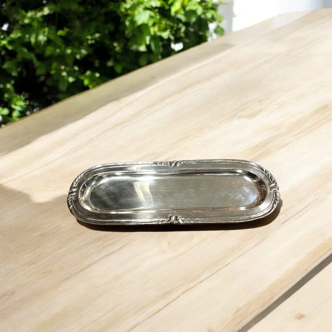 Bandeja alargada de metal plateado con detalles ornamentales. Perfecta para realzar la presentación en mesas y espacios decorativos.