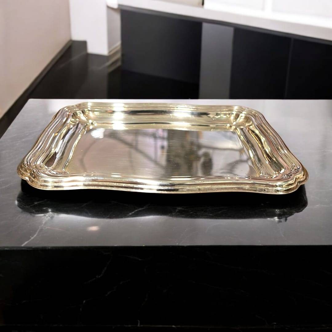 Bandeja de metal plateado con bordes ondulados y acabado brillante. Perfecta para uso decorativo en interiores sofisticados.