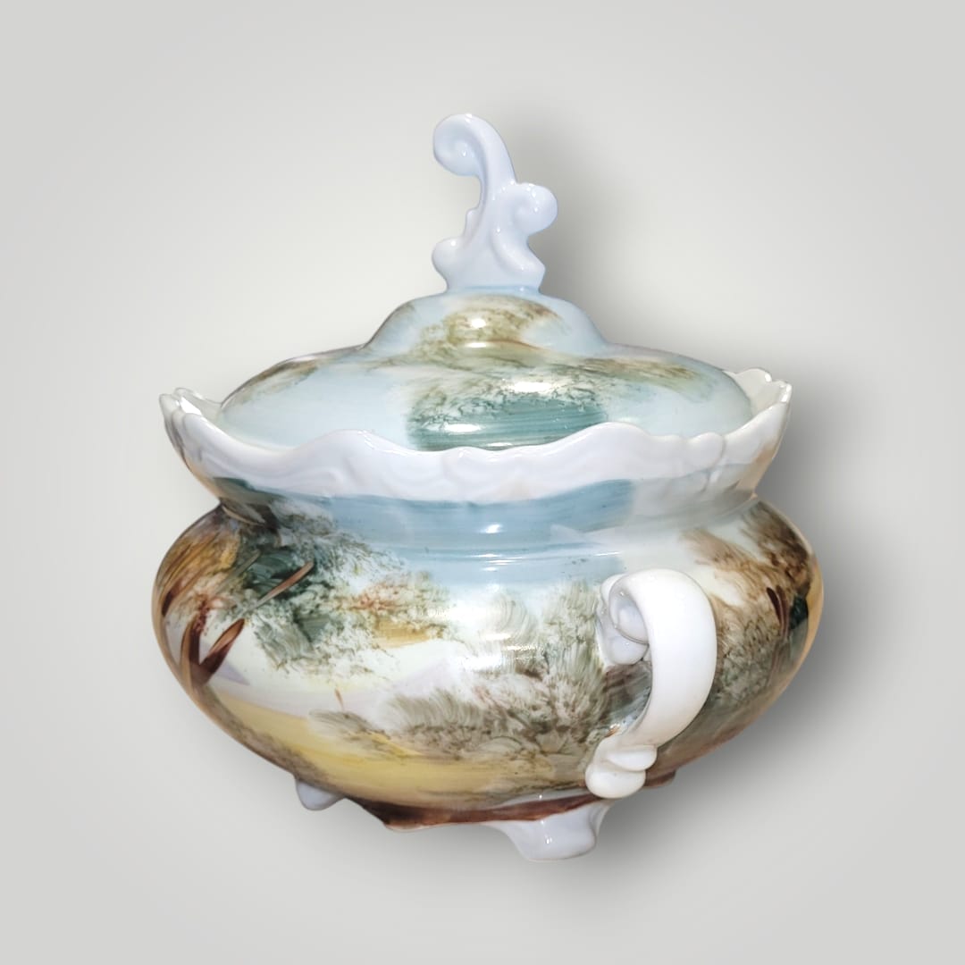 Bombonera de porcelana pintada a mano con detalles de árboles y paisajes rurales. Diseño artesanal y tapa decorativa única.