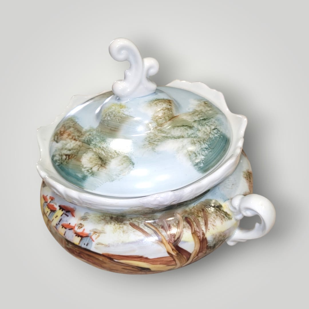 Bombonera de porcelana pintada a mano con motivos campestres, asas curvas y tapa con diseño artístico. Perfecta para decoración especial.