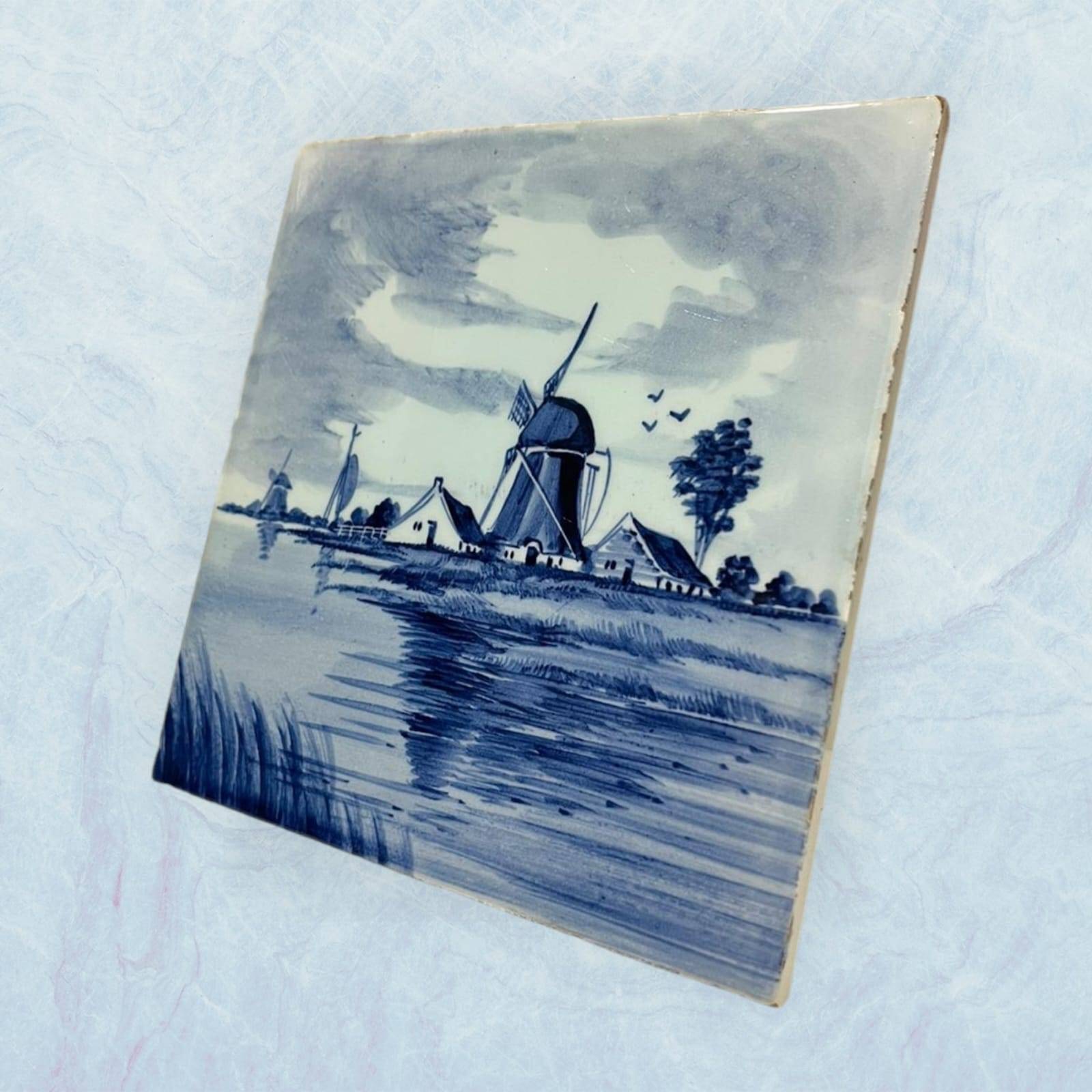 Azulejo decorativo estilo Delft Blue en perspectiva lateral, muestra escena rural holandesa con molino. Ideal para colección o decoración mural.