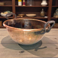 Caldero de cobre con asas de forja artesanal sobre mesa rústica.