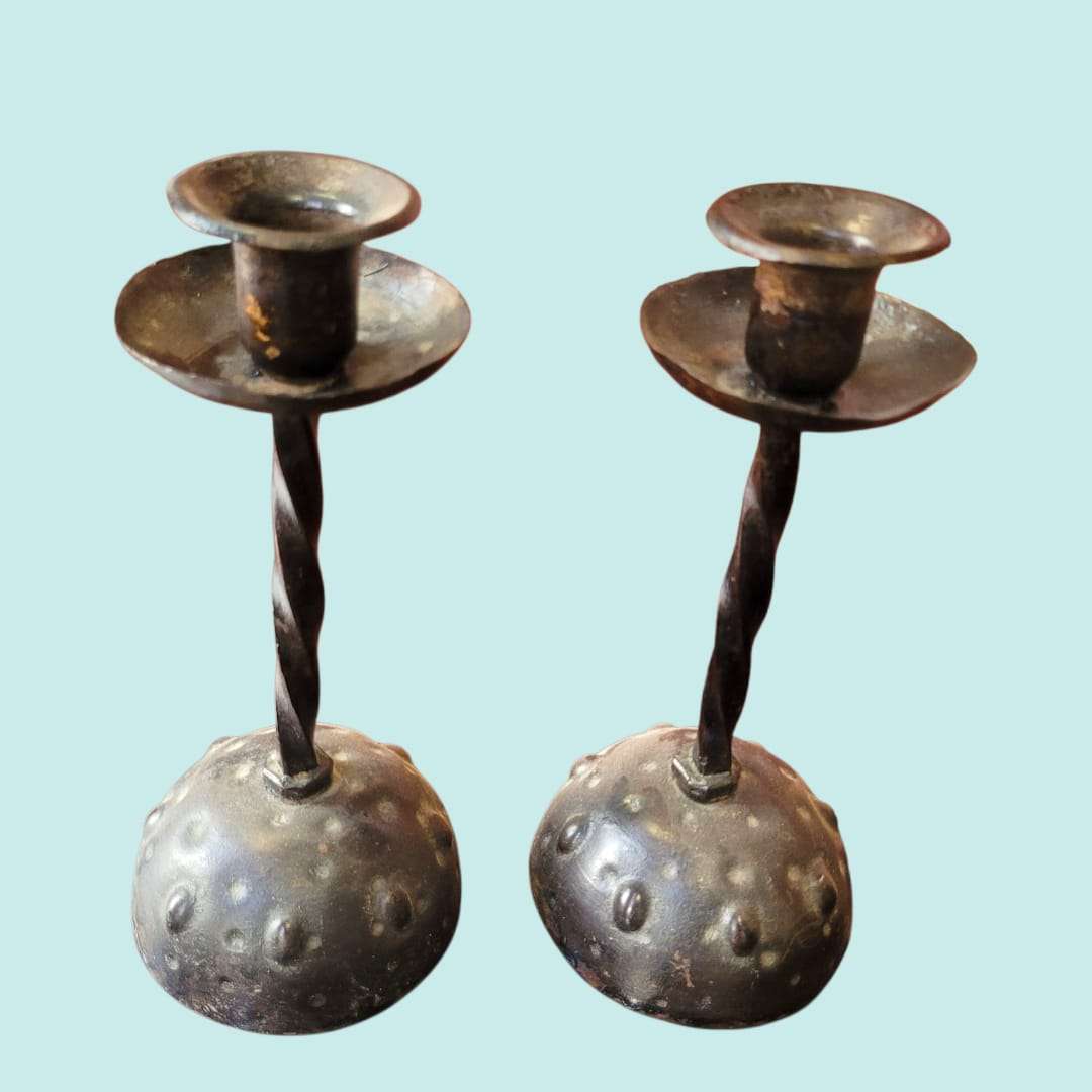 Par de candeleros de forja antigua con diseño martillado y base texturizada. Estilo rústico ideal para decoración vintage de interiores.