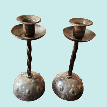 Par de candeleros de forja antigua con diseño martillado y base texturizada. Estilo rústico ideal para decoración vintage de interiores.