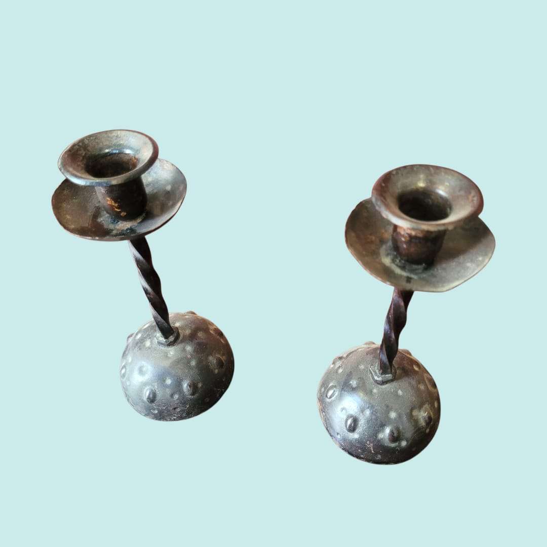 Par de candeleros de forja antigua con diseño martillado y base texturizada. Estilo rústico ideal para decoración vintage de interiores.