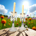 Candeleros de cristal antiguos con velas en campo florido, perfectos para ambientar espacios románticos y clásicos al aire libre.