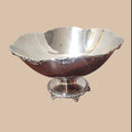 Centro de mesa de metal plateado con diseño elegante y bordes decorativos, ideal para decoración de interiores.