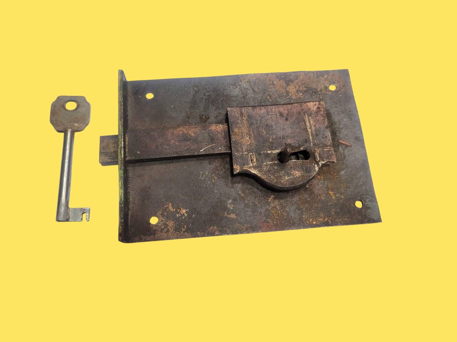 Cerradura de forja antigua con llave original colocada al lado. Perfecta para proyectos de restauración o decoración de interiores rústicos.
