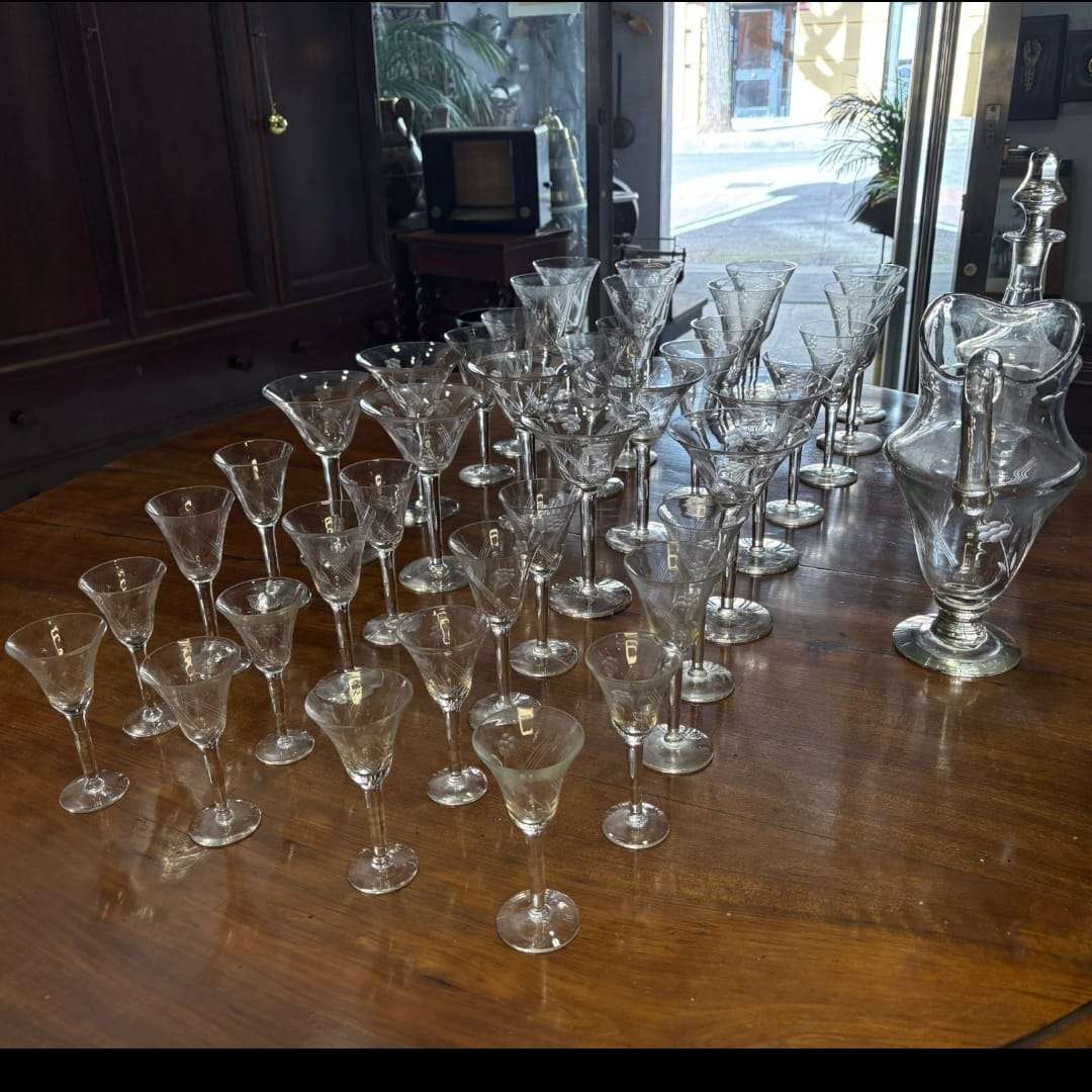 Juego completo de restos de cristalería antigua con licorera y copas talladas sobre mesa de madera, ideal para decoración clásica.