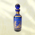 Botella de cristal cobalto con tapón esférico y ribetes dorados.