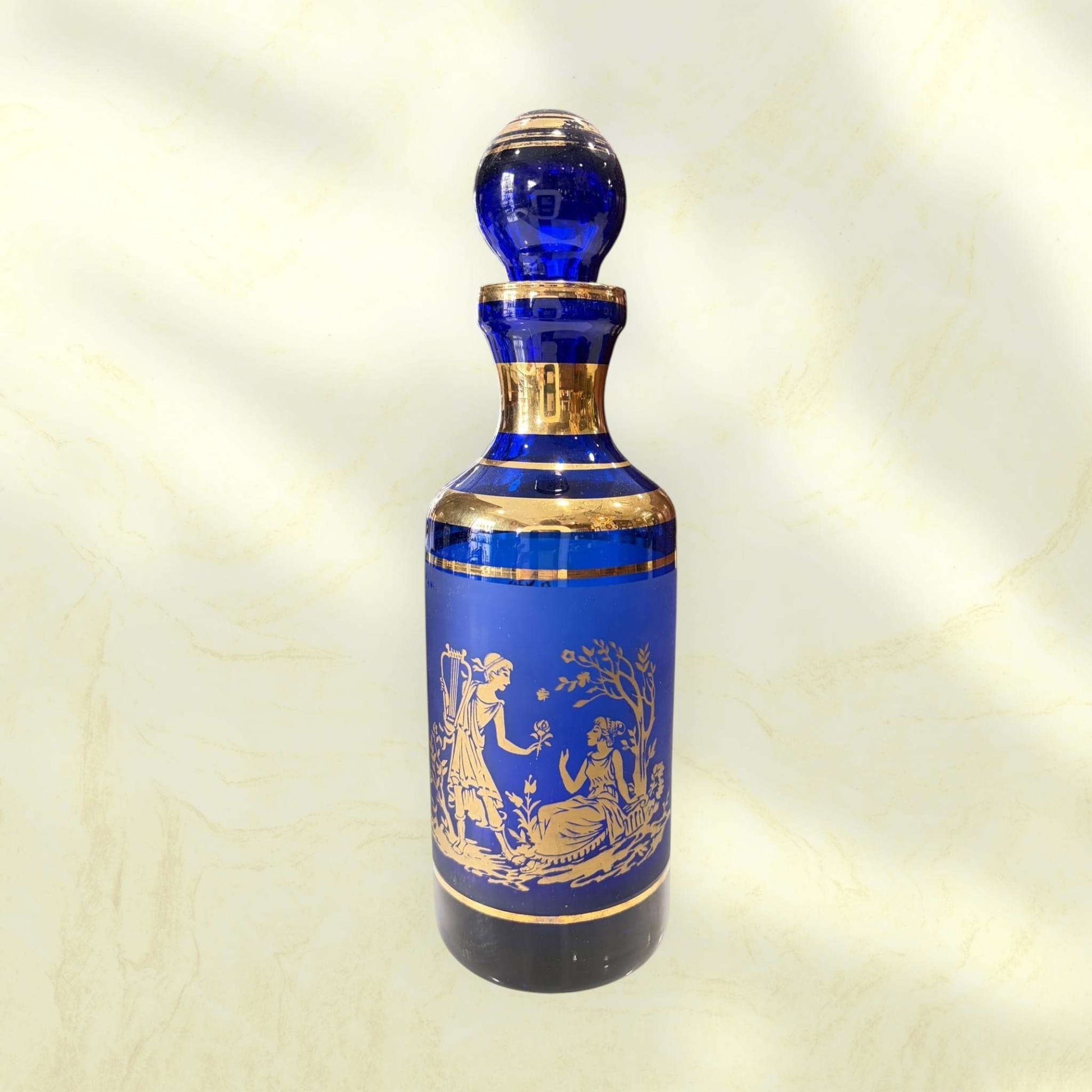 Botella de cristal cobalto con tapón esférico y ribetes dorados.