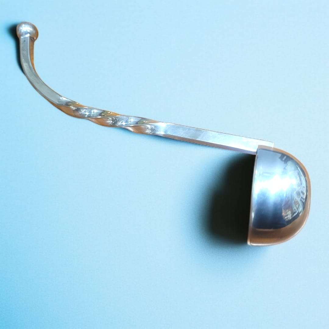 Cucharón salsero de metal plateado con diseño en espiral sobre fondo azul.