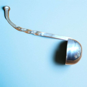 Cucharón salsero de metal plateado con diseño en espiral sobre fondo azul.