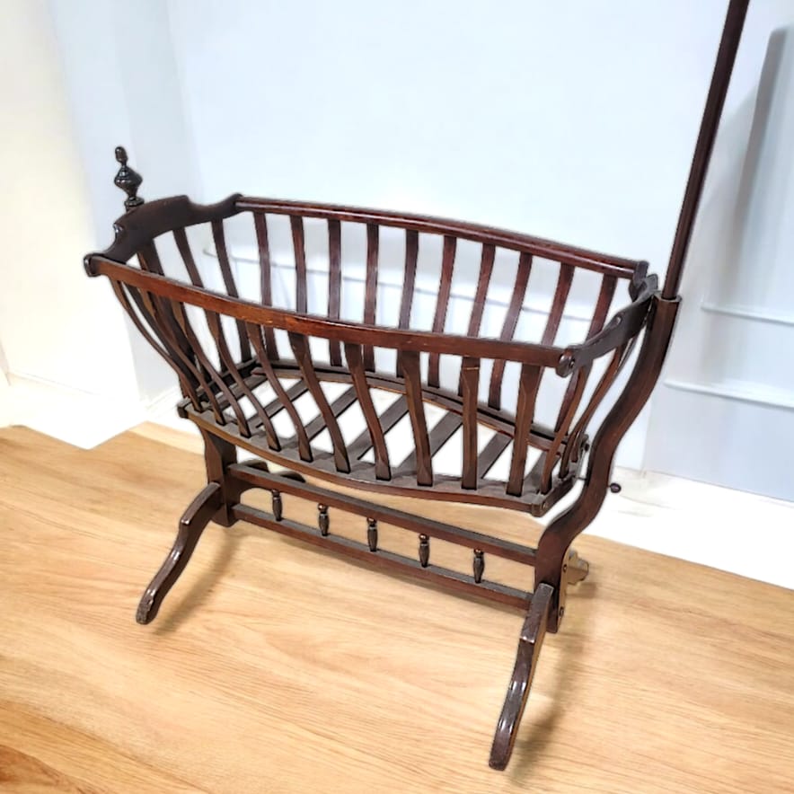 Cuna Art Nouveau de madera oscura, diseño histórico con curvas elegantes y barra superior para colgar accesorios.