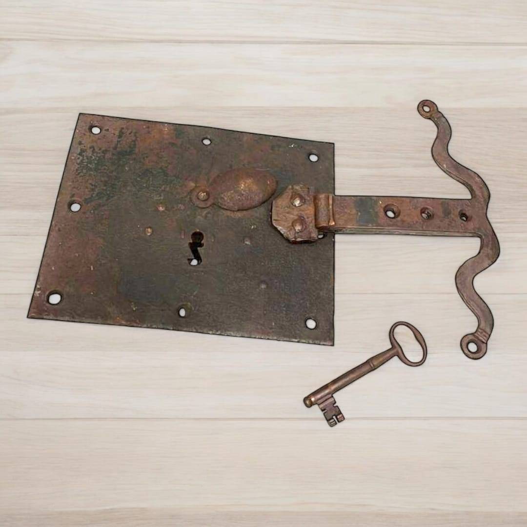 Cerradura antigua de hierro con llave incluida y detalles decorativos curvos. Accesorio decorativo para ambientes de estilo rústico y vintage.
