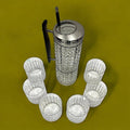 Coctelera de cristal con tapa de plata y seis vasos a juego sobre fondo verde, ideal para decoración elegante en eventos en casa.