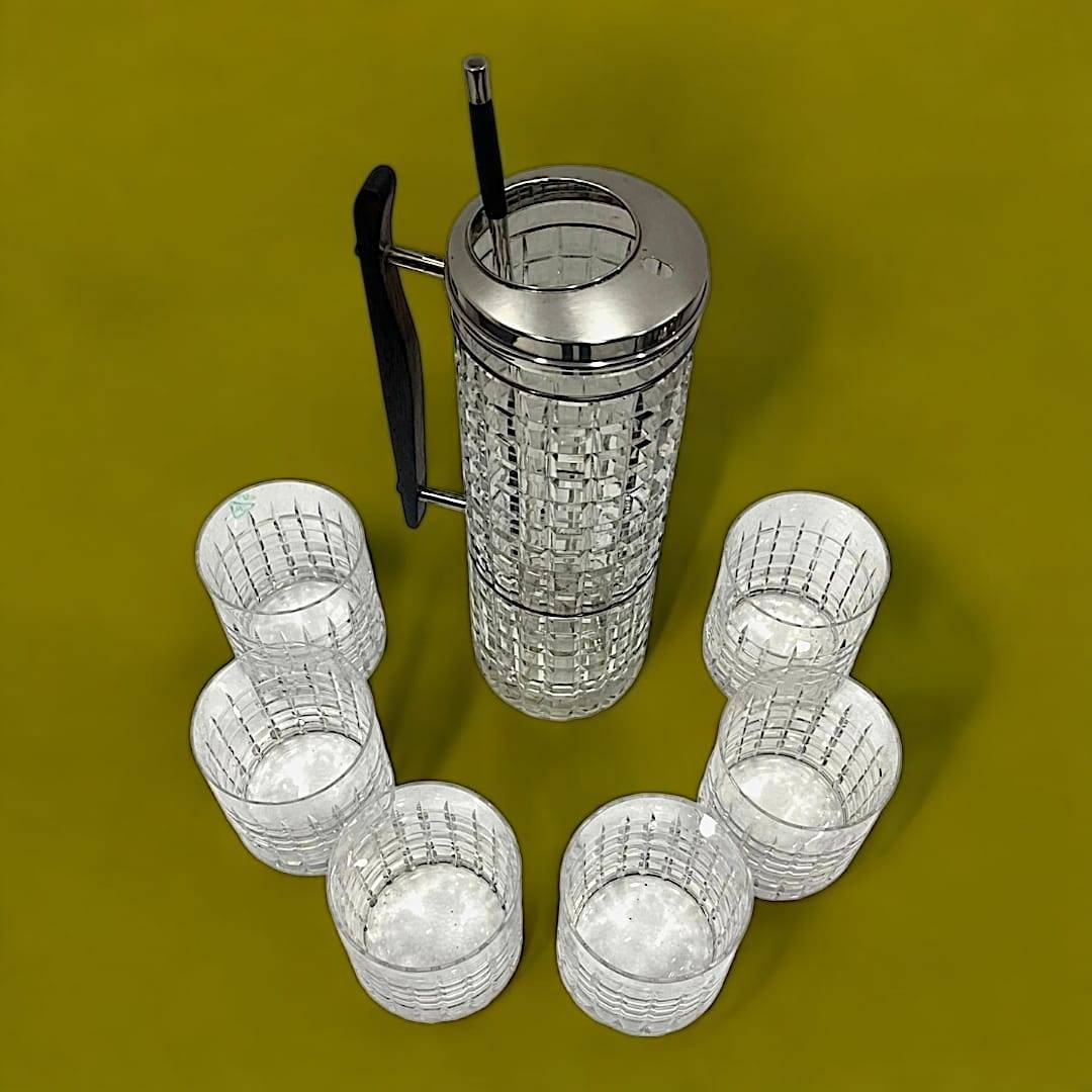 Coctelera de cristal con tapa de plata y seis vasos a juego sobre fondo verde, ideal para decoración elegante en eventos en casa.