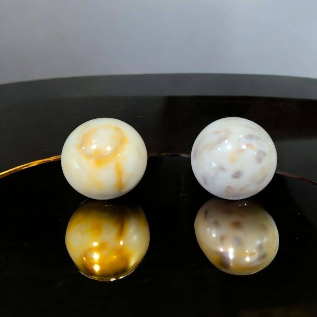 Esferas de mármol macizo decorativas para tu hogar con vetas naturales en tonos beige y blanco, sobre superficie negra brillante.