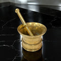 Mortero vintage en bronce con pestillo, estilo tradicional, sobre superficie negra marmoleada. Ideal para decoración clásica de cocina o comedor.