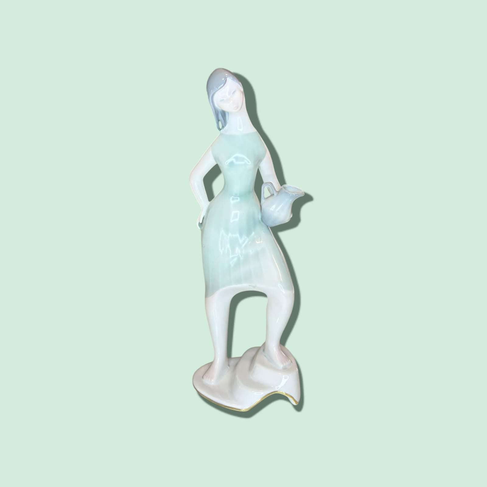 Esta exquisita Figura de porcelana, elaborada por la prestigiosa marca española Santa Clara, representa a una joven con un cántaro, interpretada en un estilo delicado, estilizado y lleno de movimiento. 