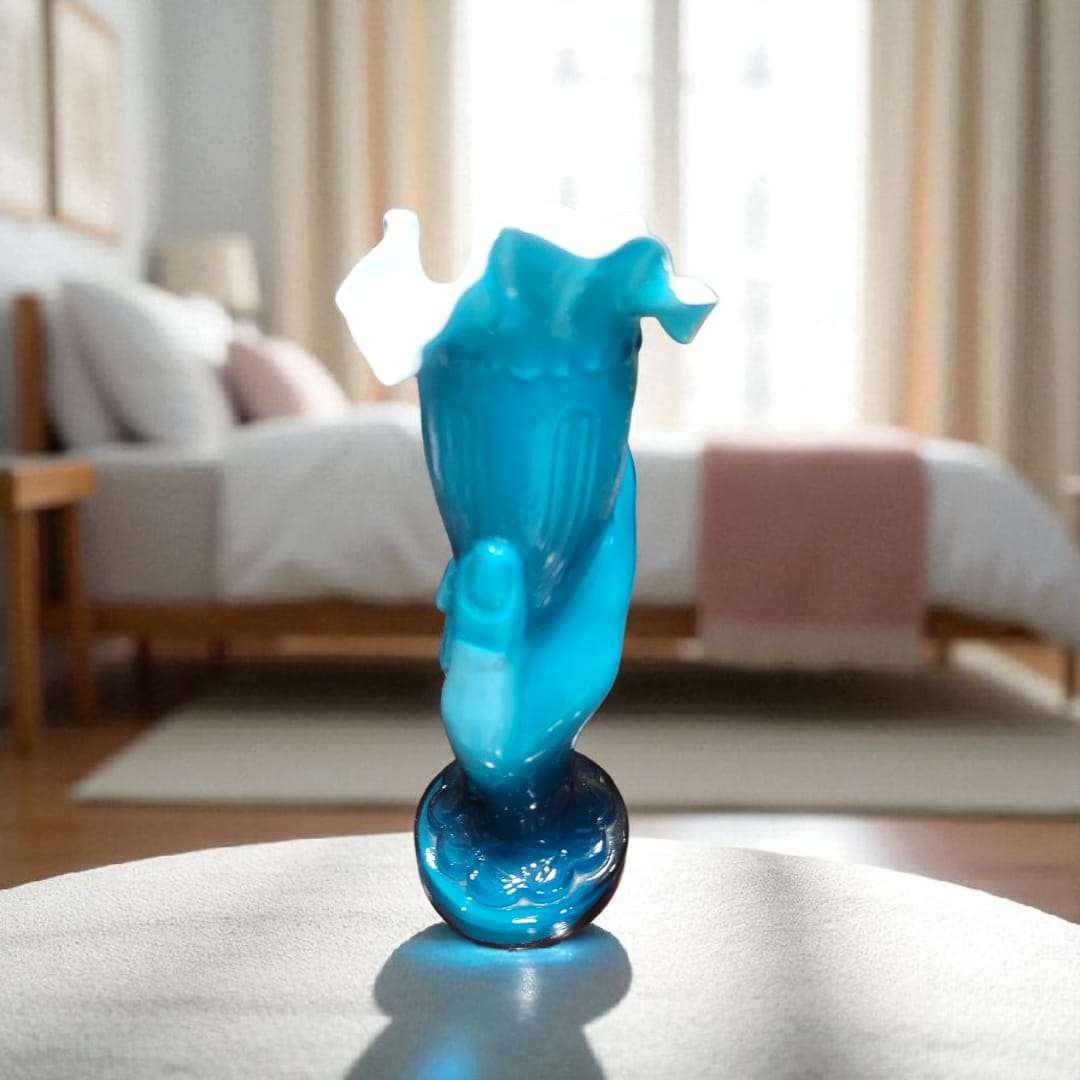 Florero de mano de cristal cuajado azul, sobre alfombra, con fondo de dormitorio.