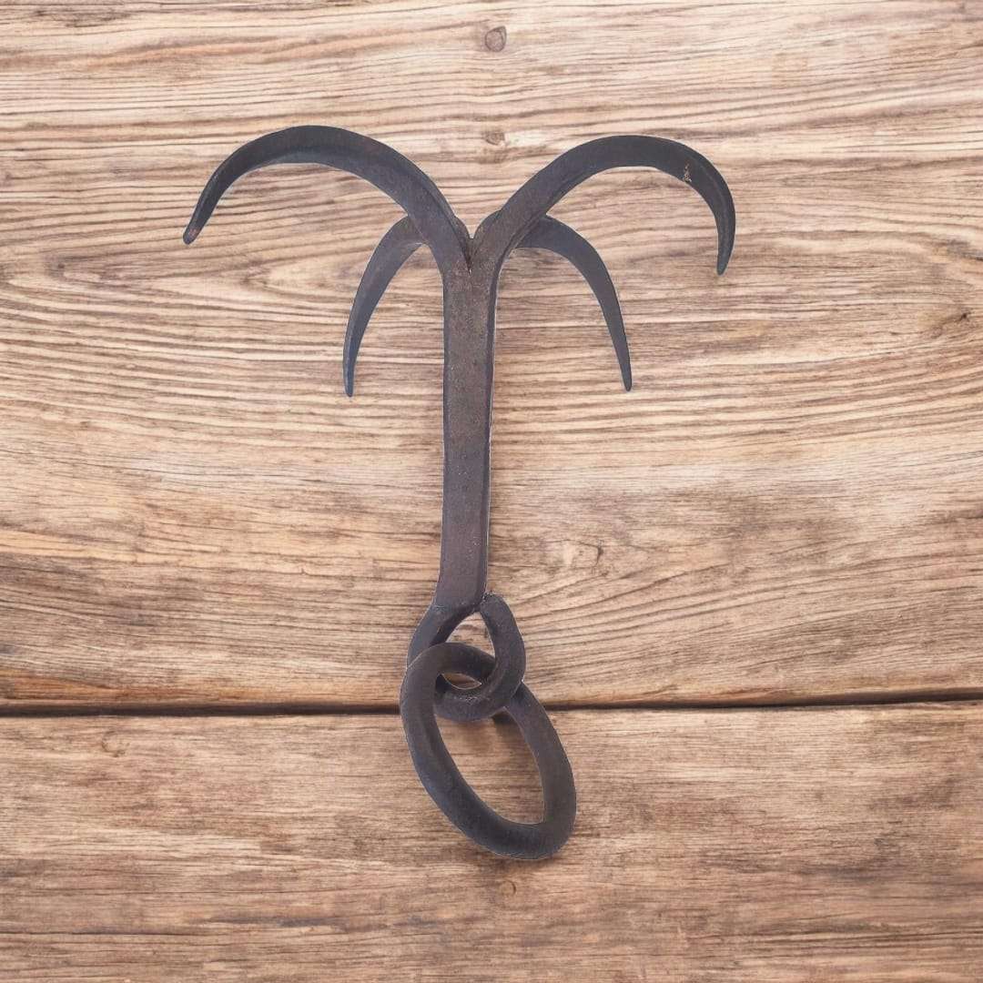 Gancho de forja extendido sobre madera, destacando su simetría y estructura.